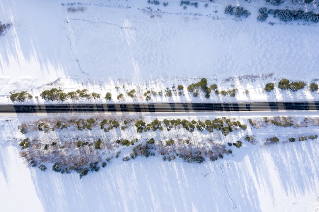 Widok z lotu ptaka na drogę otoczoną drzewami i śniegiem w świetle słonecznym