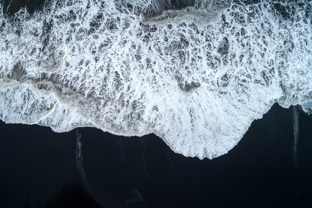 Widok z lotu ptaka na plażę z czarnym piaskiem i fale oceanu w Islandii.
