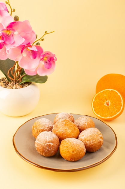 Widok z przodu cukrowe ciastka w proszku okrągłe słodkie pieczone pyszne małe ciasta na okrągłej platformie wraz z kwiatami i pokrojonymi pomarańczami i śmietaną w tle piekarnia słodkie herbatniki