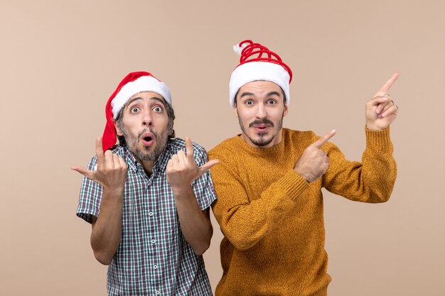 Widok z przodu dwóch mężczyzn w czapkach Świętego Mikołaja, jeden pokazuje coś, a drugi patrzy na to na odosobnionym tle