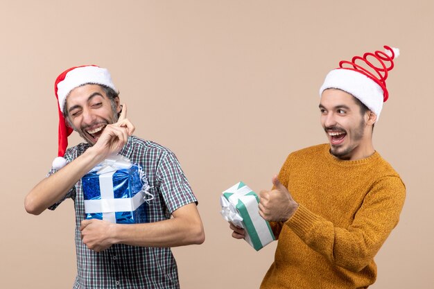 Widok z przodu dwóch szczęśliwych facetów rozmawiających i trzymających prezenty świąteczne na beżowym na białym tle