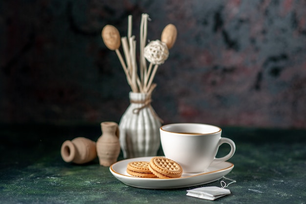 widok z przodu filiżanka herbaty z małymi słodkimi ciasteczkami na białym talerzu na ciemnej powierzchni ceremonia kolorów śniadanie rano zdjęcie szkło pić cukier