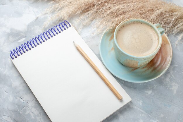 Widok z przodu filiżanka kawy z mlekiem w filiżance wraz z notesem na białym biurku pić kawę mleczną biurko kolor