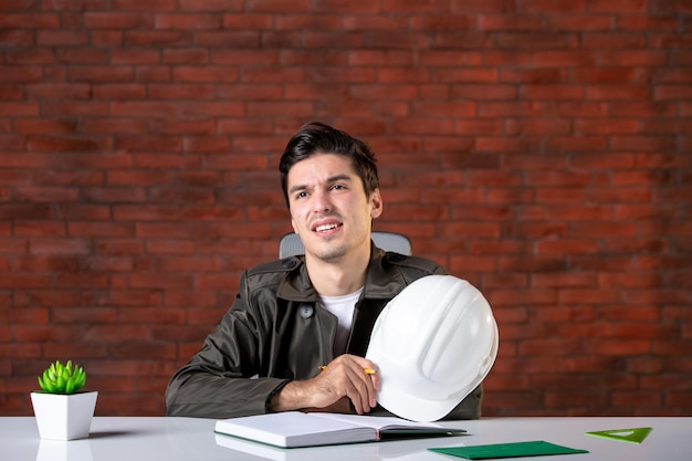 Widok z przodu inżynier-mężczyzna siedzący za swoim miejscem pracy i piszący notatki dokument plan biznes korporacyjny budowniczy nieruchomości harmonogram pracy wykonawcy