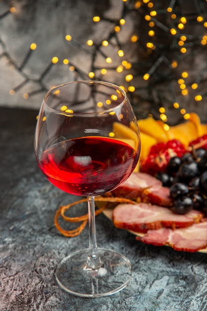 Widok z przodu kieliszek do wina winogrona kawałki sera plastry mięsa na drewnianej płycie na ciemnych światłach świątecznych