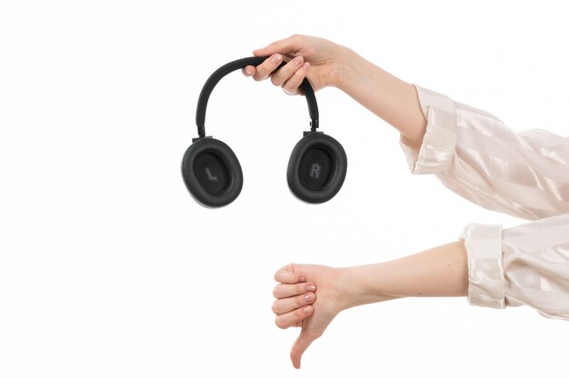 Widok z przodu kobiecej ręki trzymającej czarne słuchawki pokazujące inny znak na białym
