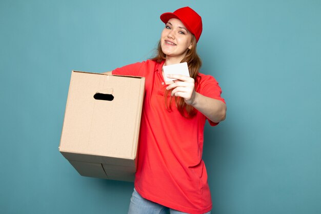 Widok z przodu kobiet atrakcyjny kurier w czerwonej koszulce polo czerwonej czapce i dżinsach, trzymając pudełko pozowanie uśmiechnięty na niebieskim tle usługi gastronomicznej