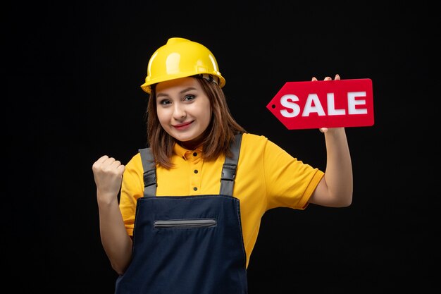 Widok z przodu kobieta budowniczy w mundurze trzymającym znak sprzedaży na czarnej ścianie