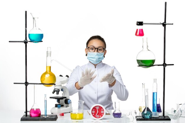 Widok z przodu kobieta chemik w białym kombinezonie medycznym z maską, siedząca na białym tle chemik wirus covid-splash lab