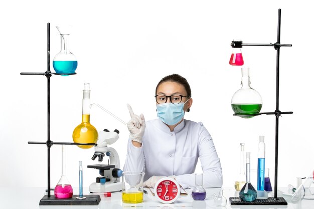 Widok z przodu kobieta chemik w białym kombinezonie medycznym z maską siedzi na białym tle chemik wirus covid-splash lab