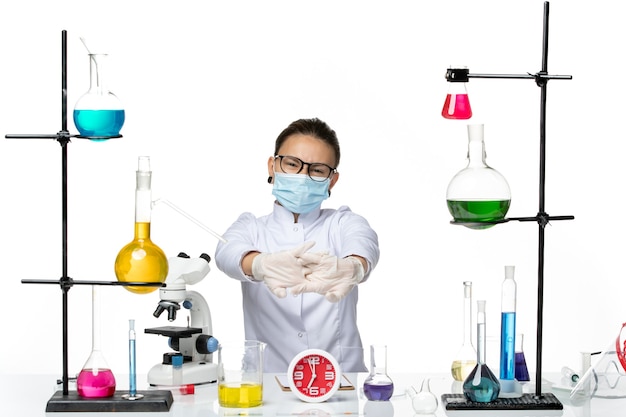 Widok z przodu kobieta chemik w garniturze medycznym z maską siedzi z roztworami na białym biurku wirus chemii plusk covid-lab
