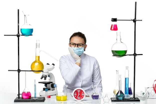 Widok z przodu kobieta chemik w garniturze medycznym z maską siedzi z roztworami na jasnym białym tle laboratorium wirusów chemii covid- splash