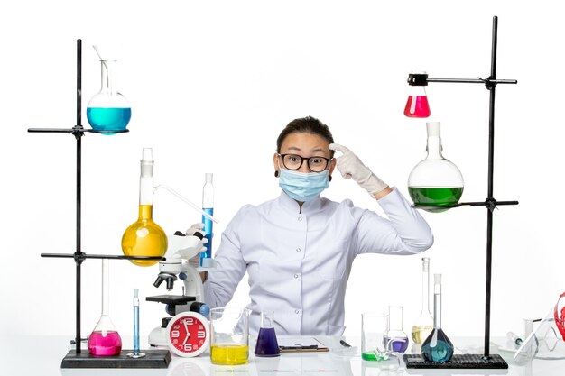 Widok z przodu kobieta chemik w garniturze medycznym z maską trzymającą kolbę z niebieskim roztworem na białym tle Laboratorium chemii wirusa covid splash