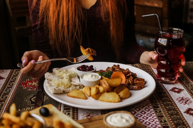 Bezpłatne zdjęcie widok z przodu kobieta jedząca smażone yamso w sosie ze smażonymi ziemniakami chleb pita i sosami na talerzu z sokiem na stole