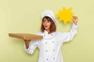 Bezpłatne zdjęcie widok z przodu kobieta kucharz w białym garniturze, trzymając pudełko na żywność i żółty znak na zielonej powierzchni