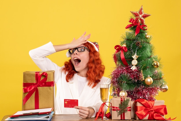 Bezpłatne zdjęcie widok z przodu kobieta lekarz posiadający kartę bankową wokół świątecznych prezentów i drzewa