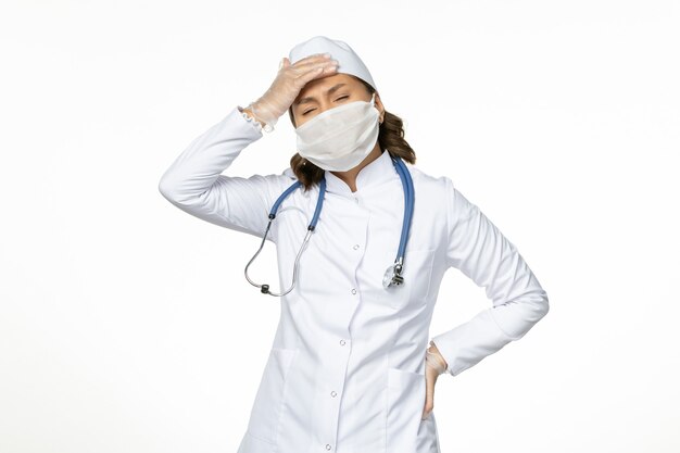 Widok z przodu kobieta lekarz w białym garniturze medycznym i masce cierpiącej na ból głowy na białym biurku lekarstwo choroba wirusowa pandemy