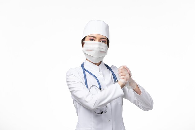 Widok z przodu kobieta lekarz w białym sterylnym kombinezonie medycznym i noszącej maskę z powodu covid- stawiania na białym biurku choroba wirusowa choroba pandemiczna