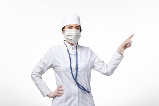 Widok z przodu kobieta lekarz w białym sterylnym kombinezonie medycznym z maską z powodu choroby zakaźnej na białej ścianie choroby wirusa choroby
