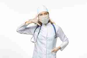 Bezpłatne zdjęcie widok z przodu kobieta lekarz w kombinezonie medycznym w masce i rękawiczkach z powodu połączenia telefonicznego koronawirusa na białym biurku pandemia wirusa choroby