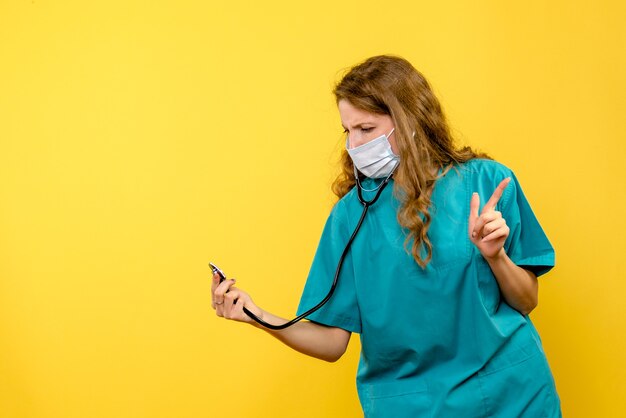 Widok z przodu kobieta lekarz w masce za pomocą stetoskopu na żółtej przestrzeni