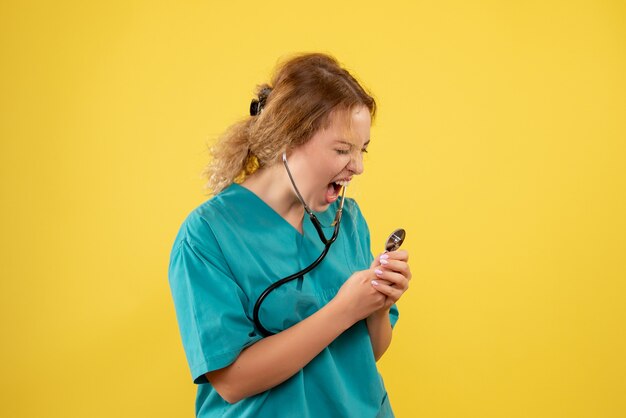 Widok z przodu kobiety lekarza w garniturze krzyczącym na stetoskop na żółtej ścianie