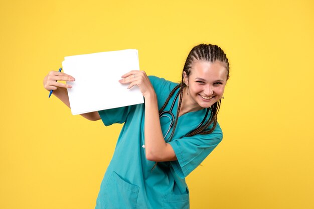 Widok z przodu kobiety lekarza w garniturze medycznym, trzymając dokumenty na żółtej ścianie