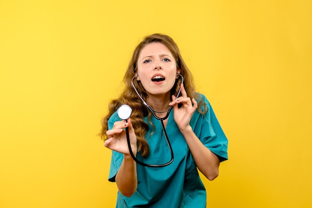 Widok z przodu kobiety lekarza za pomocą stetoskopu na żółtej ścianie