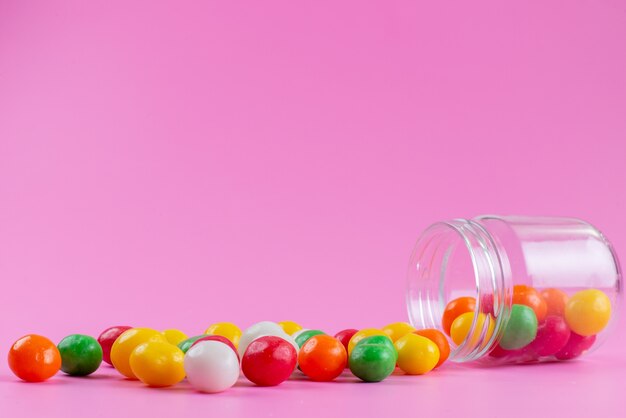 Widok z przodu kolorowe cukierki wewnątrz i na zewnątrz puszki na różowym, kolorowym słodkim cukrze