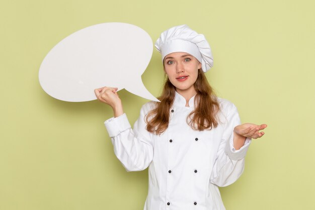 Widok z przodu kucharki na sobie biały garnitur kucharza, trzymając duży znak na zielonej ścianie