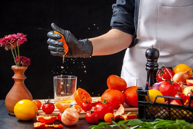 Widok z przodu kucharz robi sok mandarynkowy na czarnej sałatce zdrowy posiłek jedzenie praca dieta warzywo świeży napój owoc