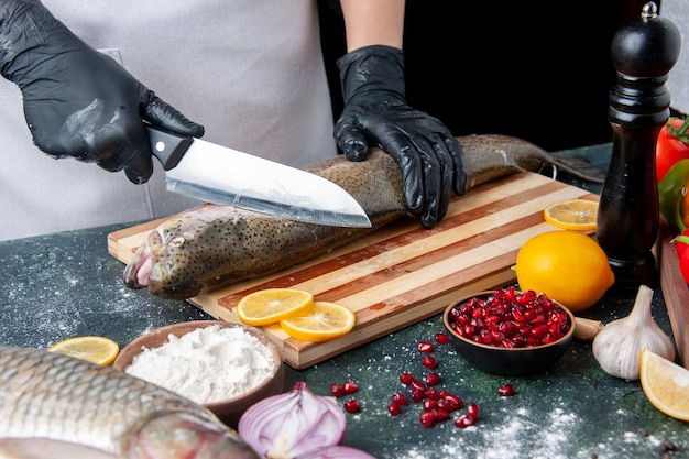 Widok z przodu kucharz sieka surową rybę na desce do mielenia pieprzu miska do mąki nasiona granatu w misce na stole kuchennym