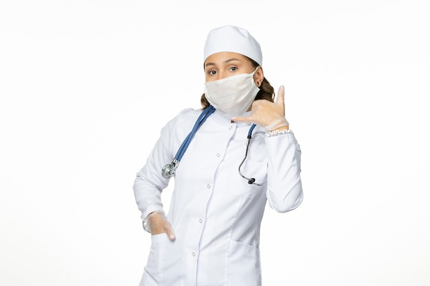 Widok z przodu lekarka w białym kombinezonie medycznym i noszącej maskę z powodu koronawirusa na białym biurku izolacja choroby pandemicznej covid