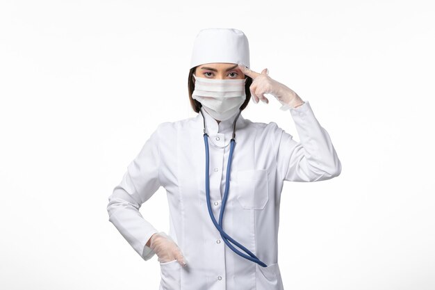 Widok z przodu lekarka w białym kombinezonie medycznym z maską z powodu koronawirusa na białej ścianie choroba choroba wirus pandemiczny covid