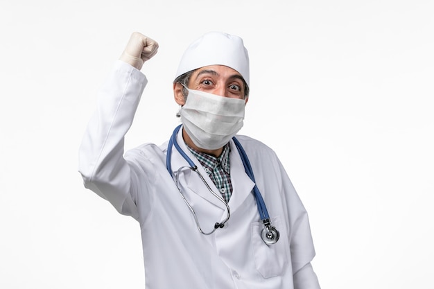 Widok z przodu lekarz mężczyzna w białym garniturze medycznym z maską z powodu covid na białym biurku