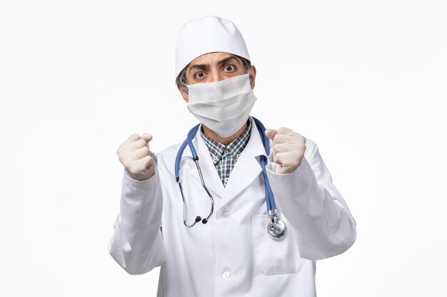 Widok z przodu lekarz mężczyzna w białym kombinezonie medycznym w masce z powodu covid na białej powierzchni