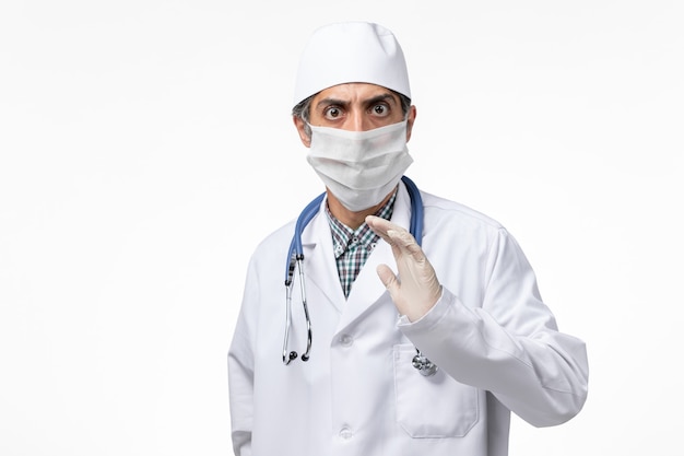 Widok z przodu lekarz mężczyzna w białym kombinezonie medycznym w masce z powodu COVID na jasnobiałym biurku