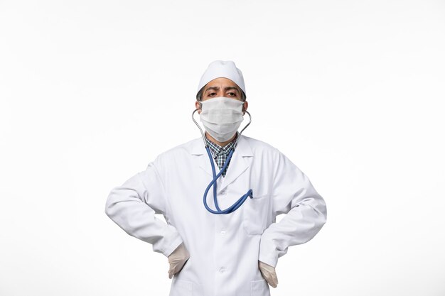Widok z przodu lekarz mężczyzna w sterylnym kombinezonie medycznym i masce z powodu koronawirusa na białej powierzchni
