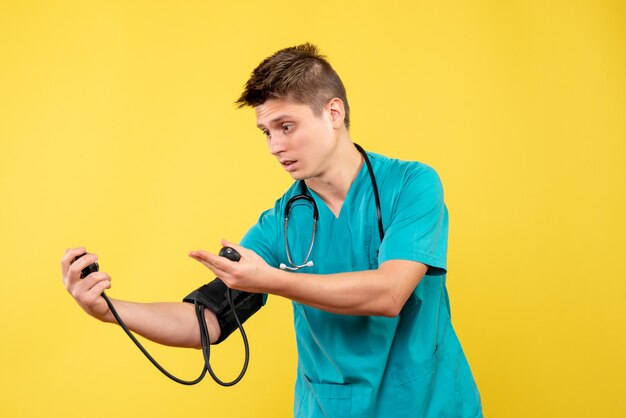 Widok z przodu lekarza płci męskiej w garniturze, sprawdzanie ciśnienia na żółtej ścianie