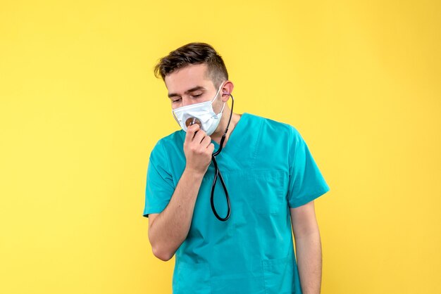 Widok z przodu lekarza ze stetoskopem i maską na żółtej ścianie