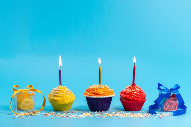 Widok z przodu małe kolorowe ciasta ze świeczkami i kokardkami na niebiesko,