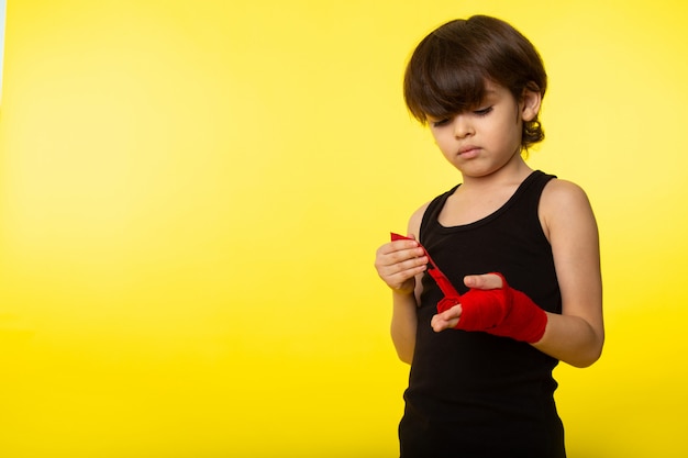 Widok z przodu małego chłopca w czarnej koszulce i związanej dłoni z czerwoną chusteczką na żółtej ścianie
