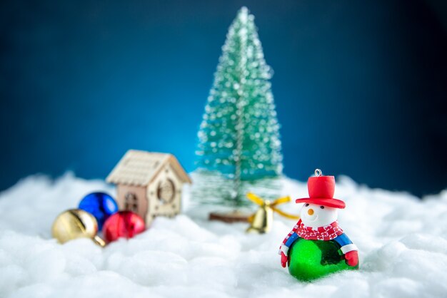 Widok z przodu mały bałwan bożonarodzeniowy drewniany dom zabawki kulkowe na niebieskiej izolowanej powierzchni