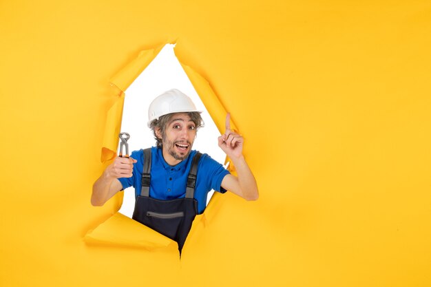 Widok z przodu męski budowniczy trzymający szczypce na żółtym tle