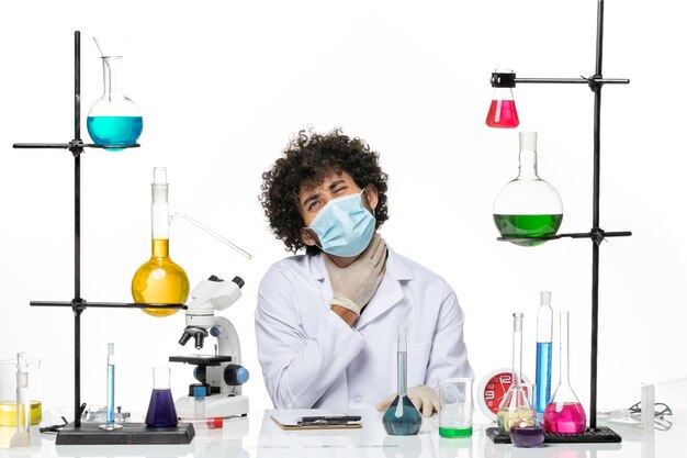Widok z przodu męski chemik w garniturze medycznym iz maską po prostu siedzący z roztworami na białej przestrzeni