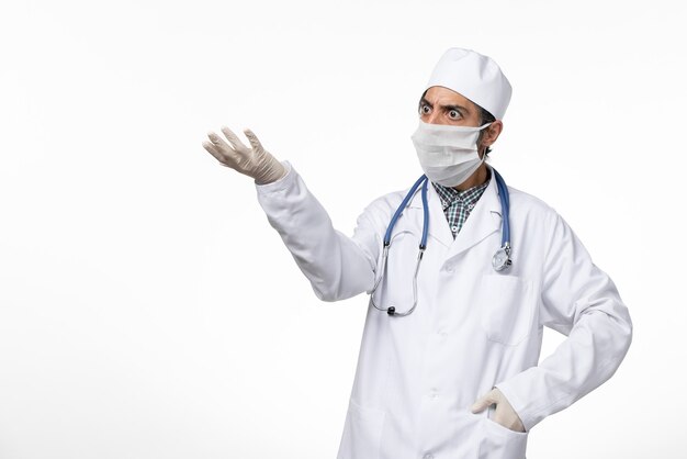 Widok z przodu męski lekarz w białym garniturze i masce z powodu koronawirusa na białej powierzchni
