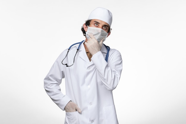 Widok z przodu męski lekarz w kombinezonie medycznym i noszący maskę jako ochrona przed covid - myślenie na białej ścianie wirus choroby - pandemia