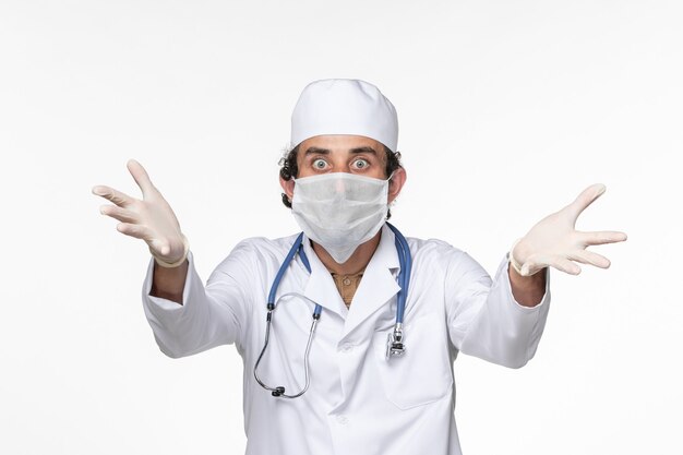 Widok z przodu męski lekarz w kombinezonie medycznym noszący sterylną maskę jako ochrona przed covid na białym biurku wirus pandemii koronawirusa