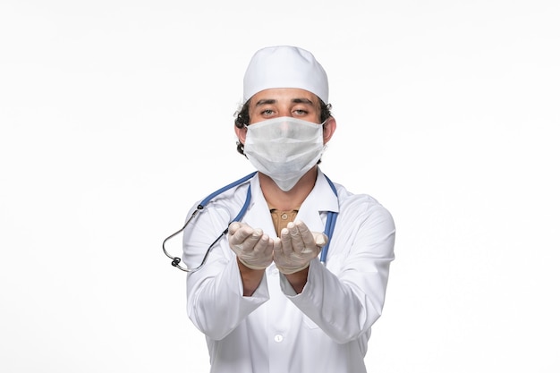 Widok z przodu męski lekarz w kombinezonie medycznym z maską jako ochrona przed covid na białej ścianie wirus pandemii koronawirusa