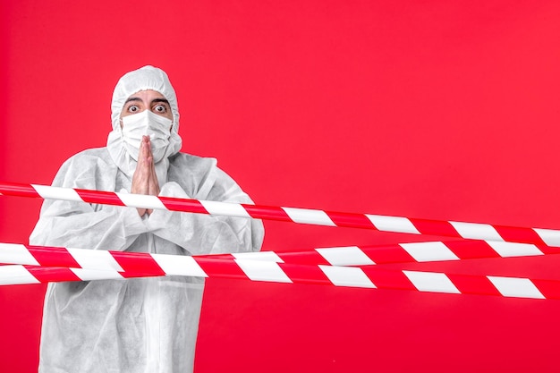 Widok z przodu męski lekarz w kombinezonie ochronnym i masce modlącej się na czerwonym tle wirus zdrowie lekarstwo szpital covid ostrzeżenie o izolacji kwarantanny